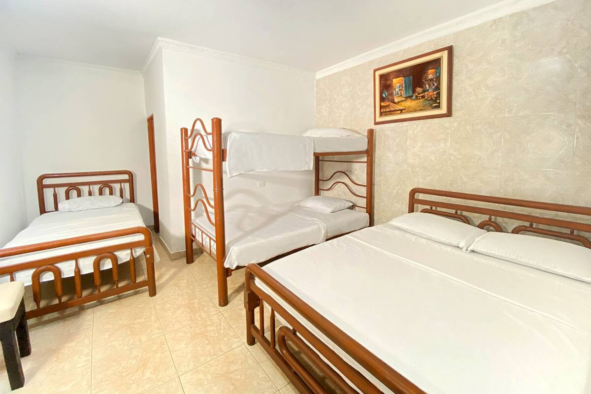 A room with three wooden beds arranged in a corner, a small table, and a painting on the wall.