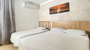 A hotel room with two single beds, a wooden headboard, a wall-mounted air conditioner, and a sunset painting. - Ayenda Republicano Colonial No 2 (Santa Marta)