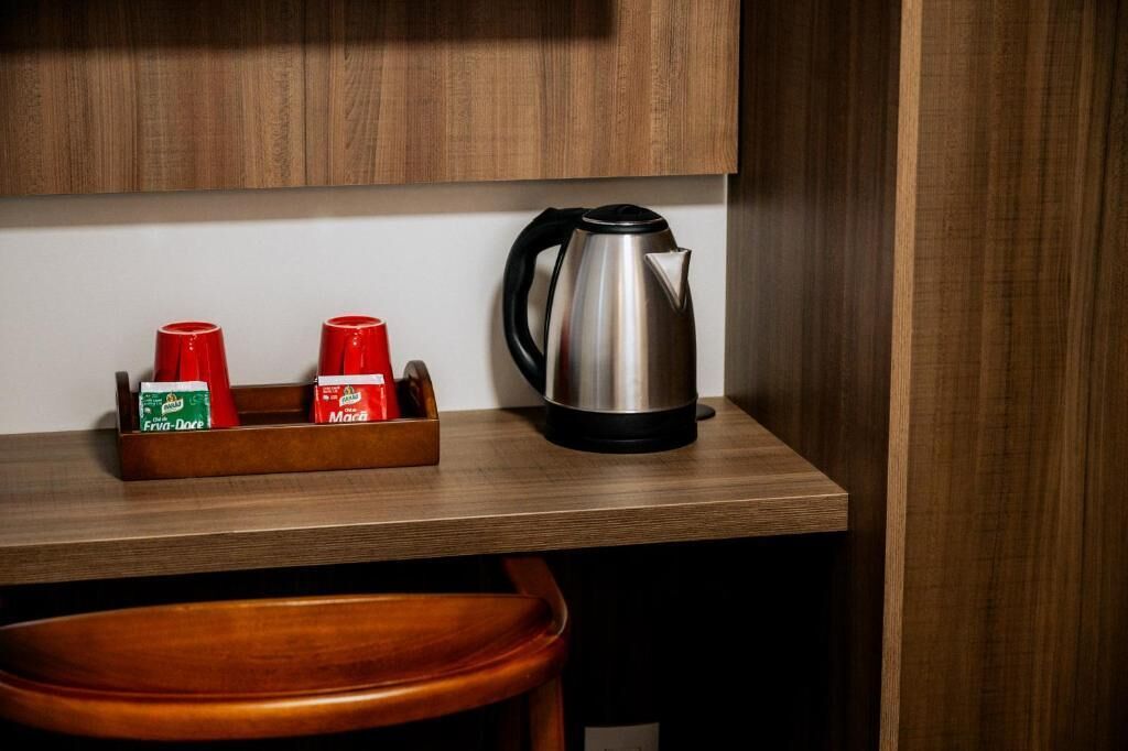 Een houten aanrecht met een roestvrijstalen waterkoker en een houder voor kruiden, met daarin twee rode bekers en twee zakjes kruiden.