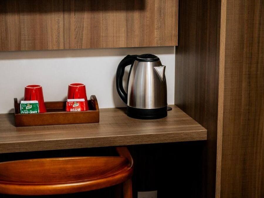 Een houten aanrecht met een roestvrijstalen waterkoker en een houder voor kruiden, met daarin twee rode bekers en twee zakjes kruiden.