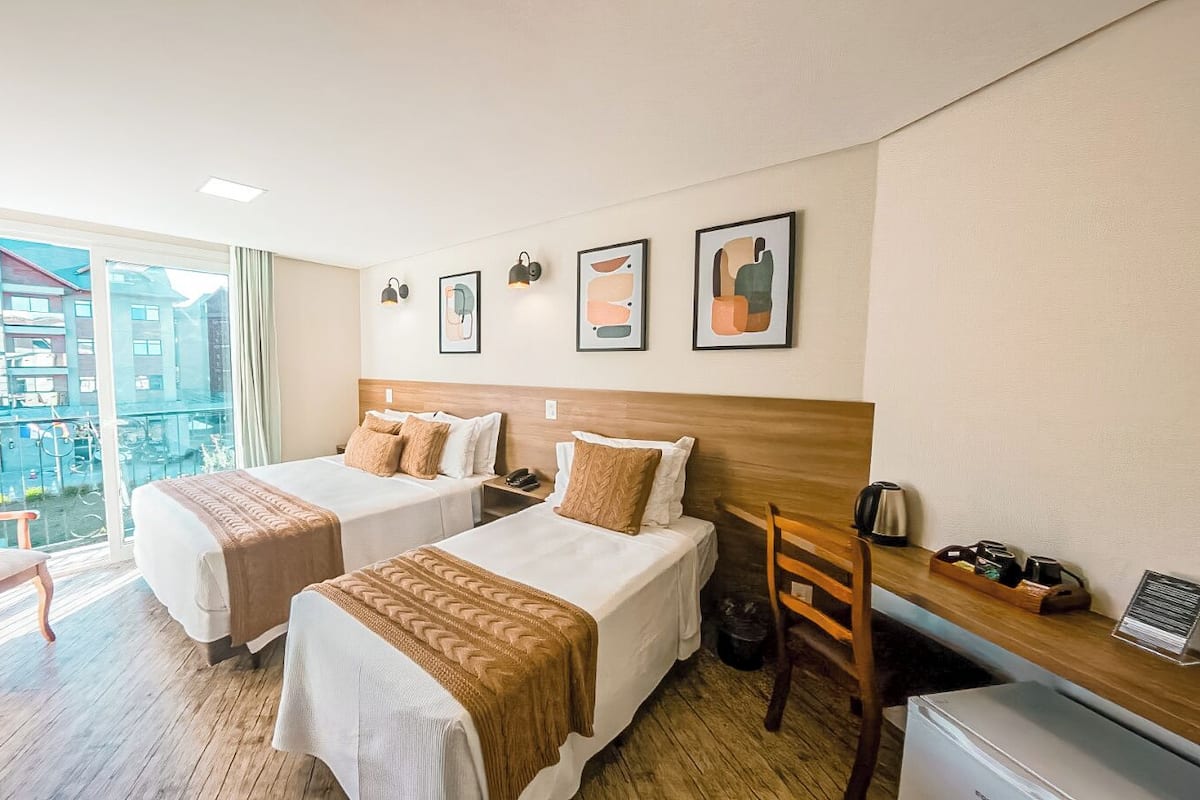 A hotel room with two beds, a desk, a chair, a coffee maker, and artwork on the wall.