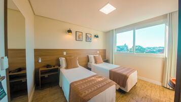 Habitación de hotel con dos camas, cabecera de madera, mesita de noche, ventana con vistas y obra de arte en la pared.