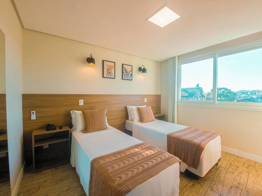 Habitación de hotel con dos camas, cabecera de madera, mesita de noche, ventana con vistas y obra de arte en la pared.