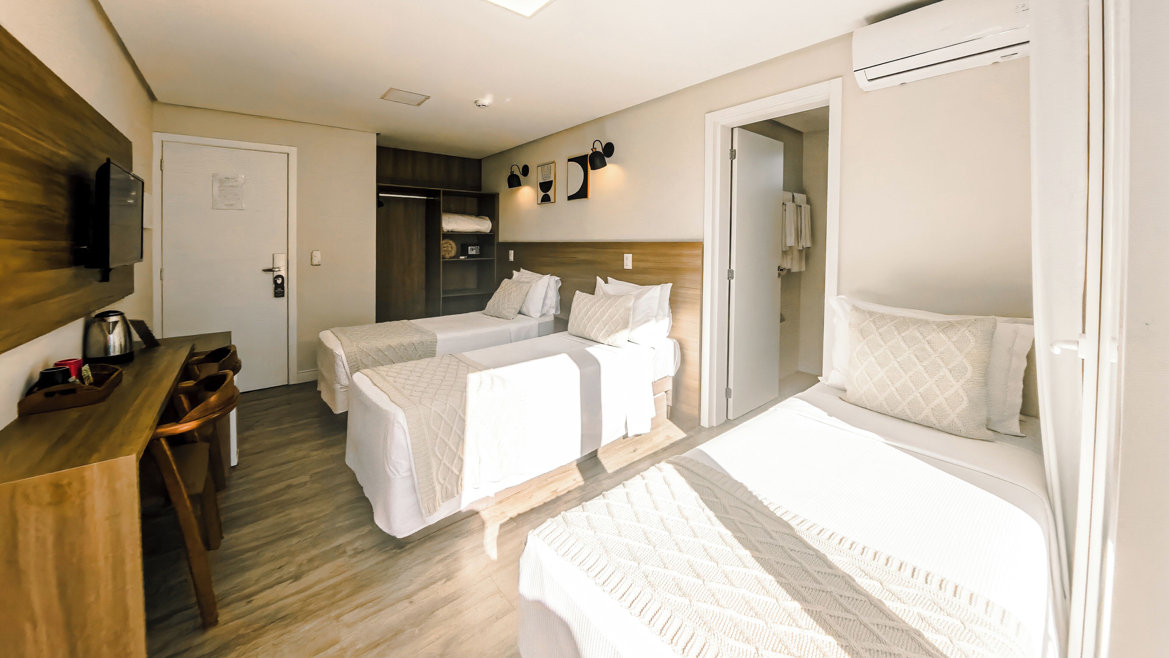 Une chambre d’hôtel avec deux lits, un bureau avec une bouilloire, une armoire et un espace douche.