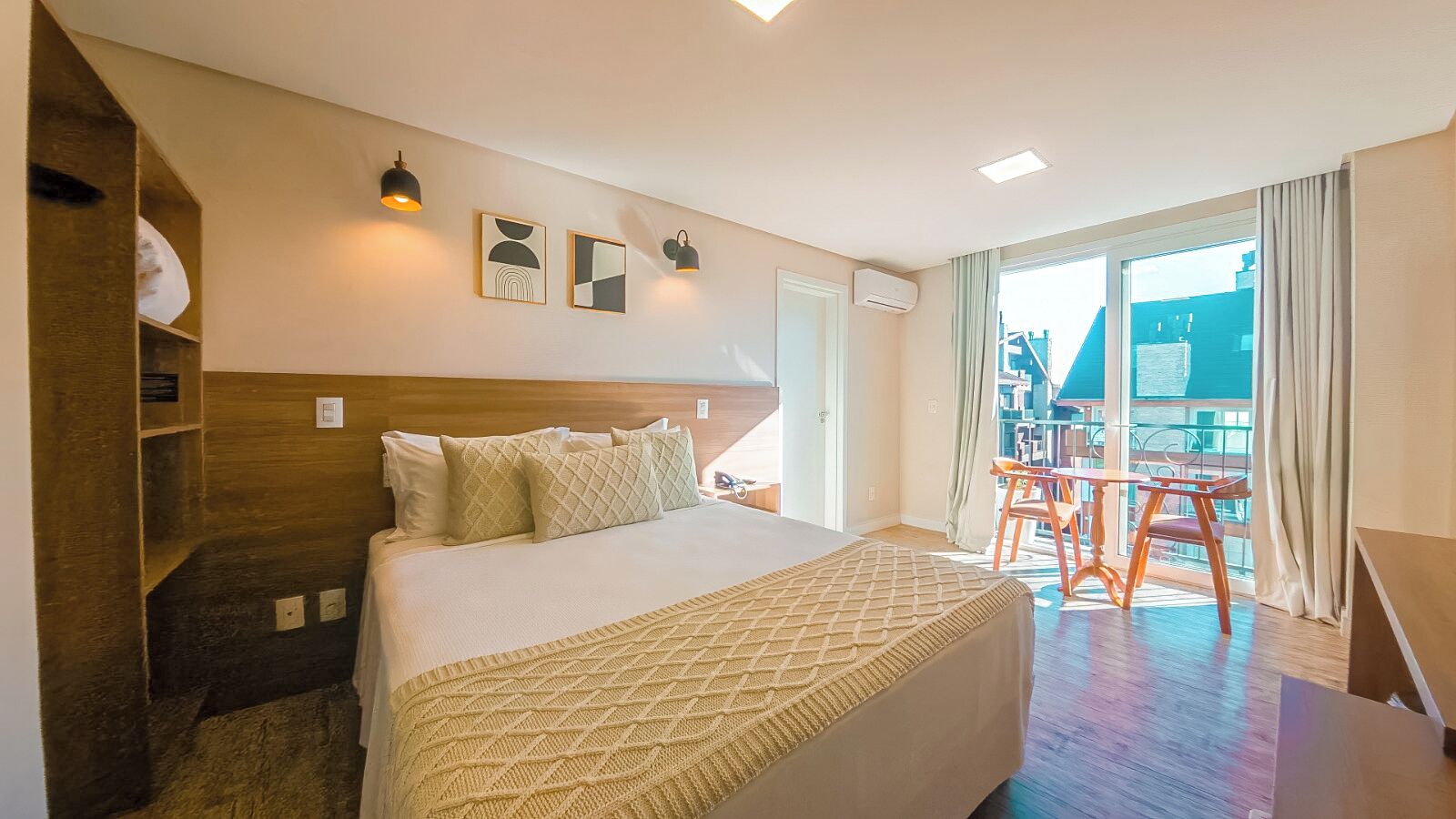 Een hotelkamer met een bed, een houten hoofdbord, een balkon met een stoel en kunst aan de muur.
