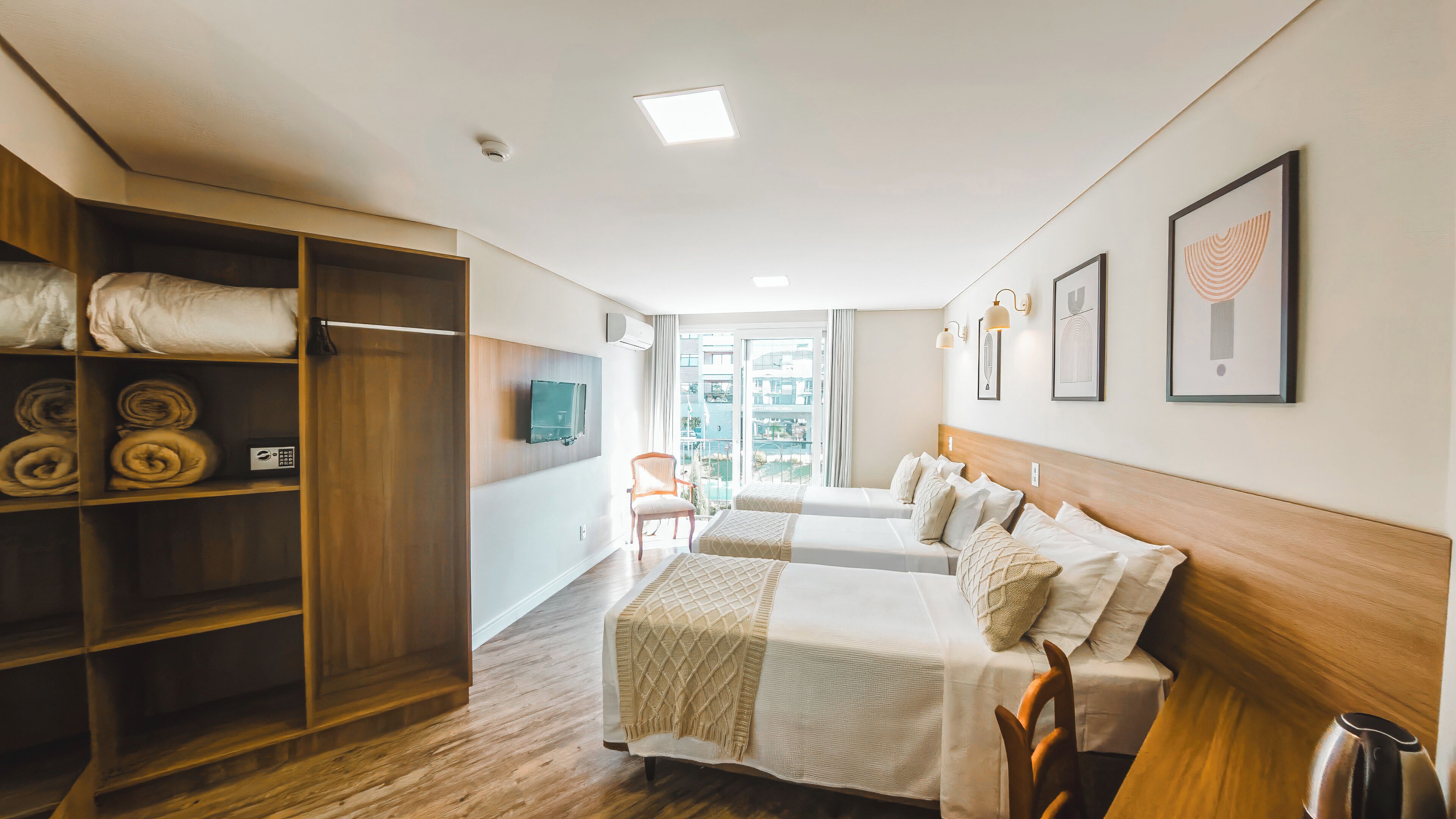 A hotel room with a bed, a wardrobe, a television, and a view of the outside.