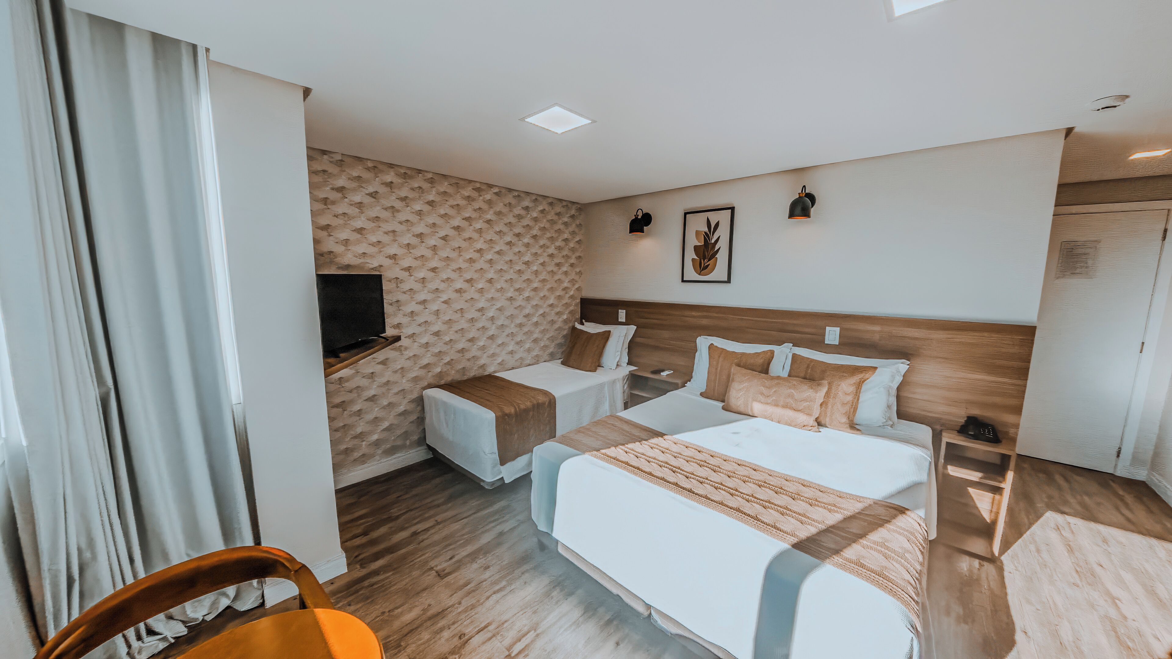 Hotellihuone, jossa on kaksi sänkyä, televisio, yöpöytä, tuoli ja puulattia.