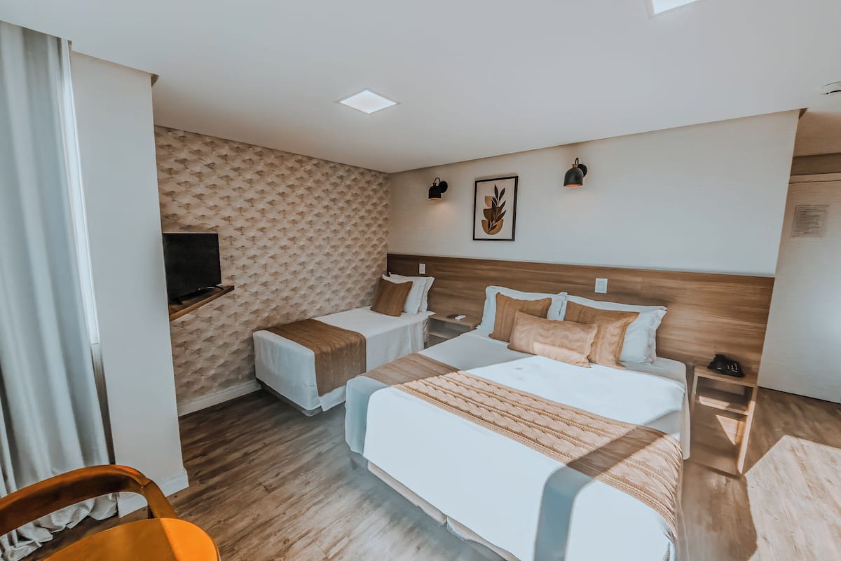 A hotel room with two beds, a TV, a bedside table, a chair, and a wooden floor.