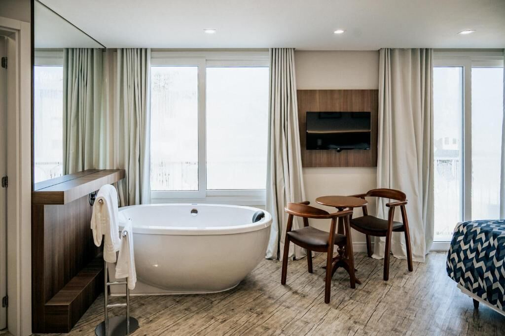 Un baño moderno con una bañera independiente, un tocador de madera, un espejo y una zona de estar con dos sillones.
