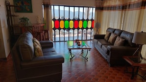 Una sala de estar con dos sofás de cuero, una mesa de centro de vidrio y vistas a través de una ventana con paneles de colores.