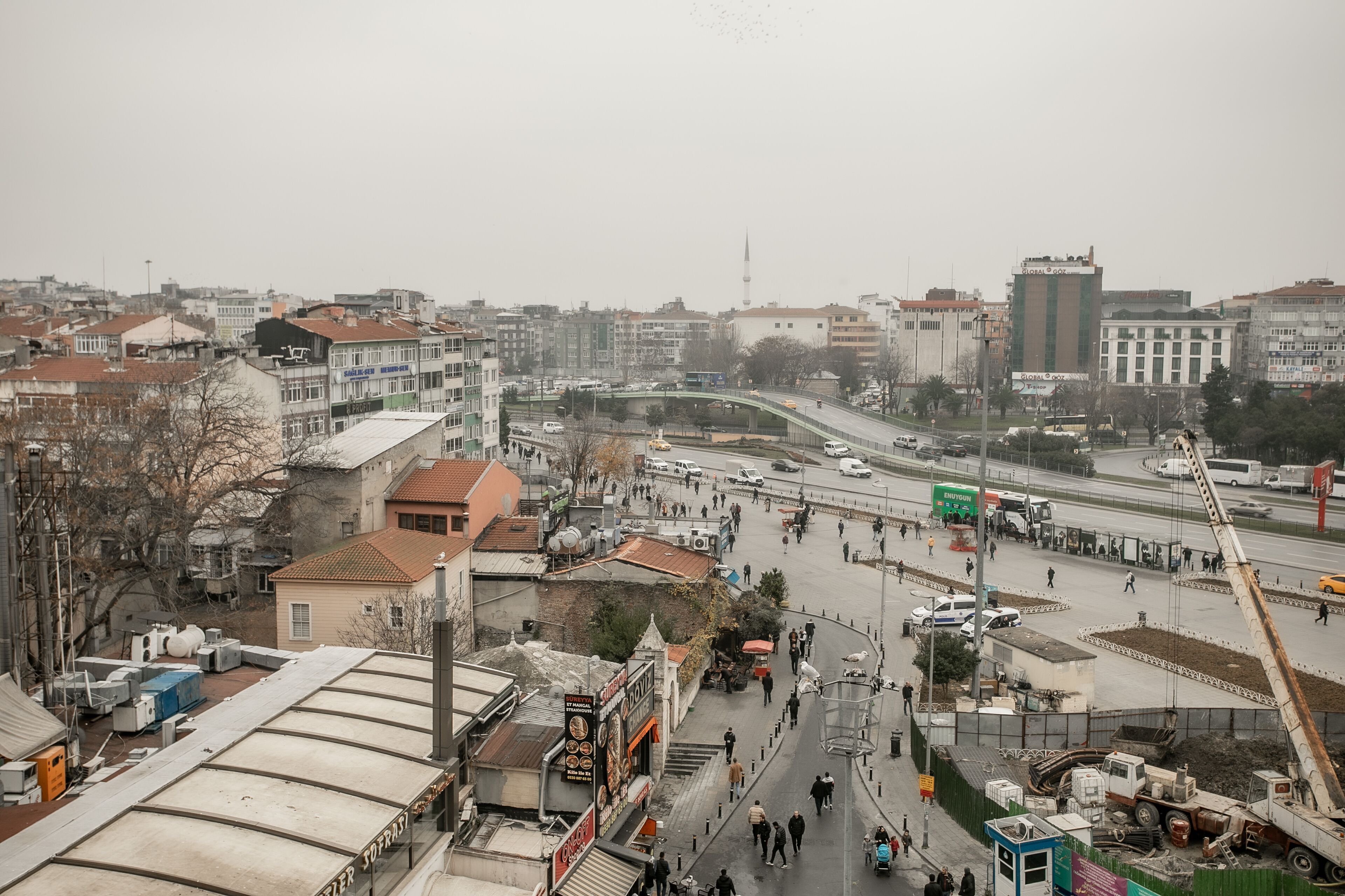 A cityscape with a prominent building with a green and white facade, a busy street with pedestrians and vehicles, and a bridge in the background.