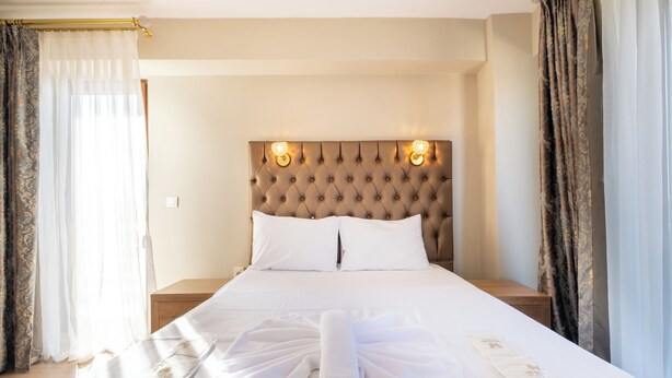 Una cama bien hecha con ropa de cama y toallas blancas, un cabecero capitonado y dos lámparas de pared.