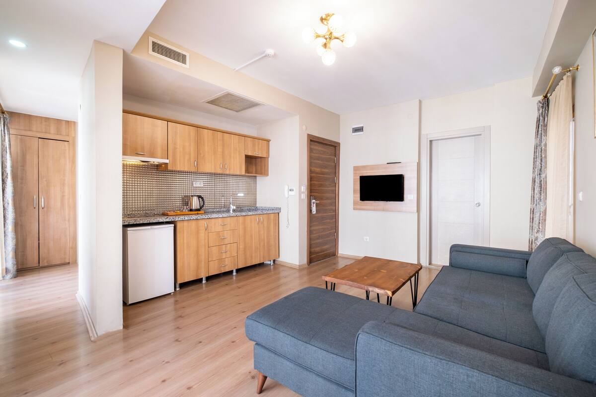 A modern apartment with a kitchenette, a grey sofa, and a wooden dining table.