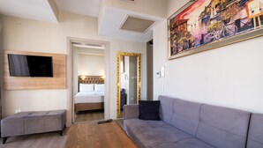 Una habitación de hotel moderna con un sofá gris, una mesa de centro de madera, un televisor de pantalla plana y un cuadro con una escena costera.