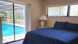 A bedroom with a bed, a lamp, and a view of a swimming pool through a glass door. - Osprey Preserve - spacious home overlooking Oscar Scherer Park (Nokomis)
