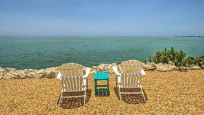 Two white Adirondack chairs and a small green table on a pebbled beach with a view of the ocean. - Direct Oceanfront Private Paradise - Pool/Spa/Dock (Marathon)