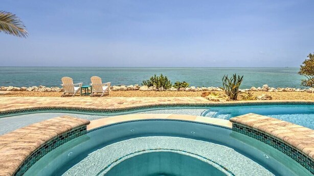 A swimming pool with a curved design, surrounded by a pebble beach and a view of the ocean. - Direct Oceanfront Private Paradise - Pool/Spa/Dock (Marathon)