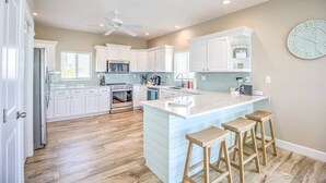 A modern kitchen with white cabinets, a central island with stools, a ceiling fan, and a clock on the wall. - Direct Oceanfront Private Paradise - Pool/Spa/Dock (Marathon)
