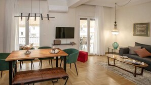 A modern living room with a wooden dining table, green chairs, a sofa, and a TV. - 3 bedroom apt next to Syntagma with Acropolis view, Luxury Apartment (Athens)