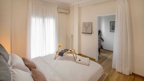 A bedroom with a bed, a bedside table with a glass of orange juice, a framed picture, and a door leading to another room. - 3 bedroom apt next to Syntagma with Acropolis view, Luxury Apartment (Athens)
