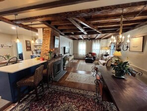 Un vaste espace de vie comprenant un grand coin repas avec une table en bois, une cheminée et un coin cuisine avec un mur en briques.