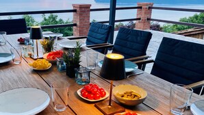 Mesa lista para comer con platos, vasos y una vela, con vistas a un cuerpo de agua.