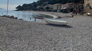 Una playa pedregosa con un bote, edificios y una colina al fondo.