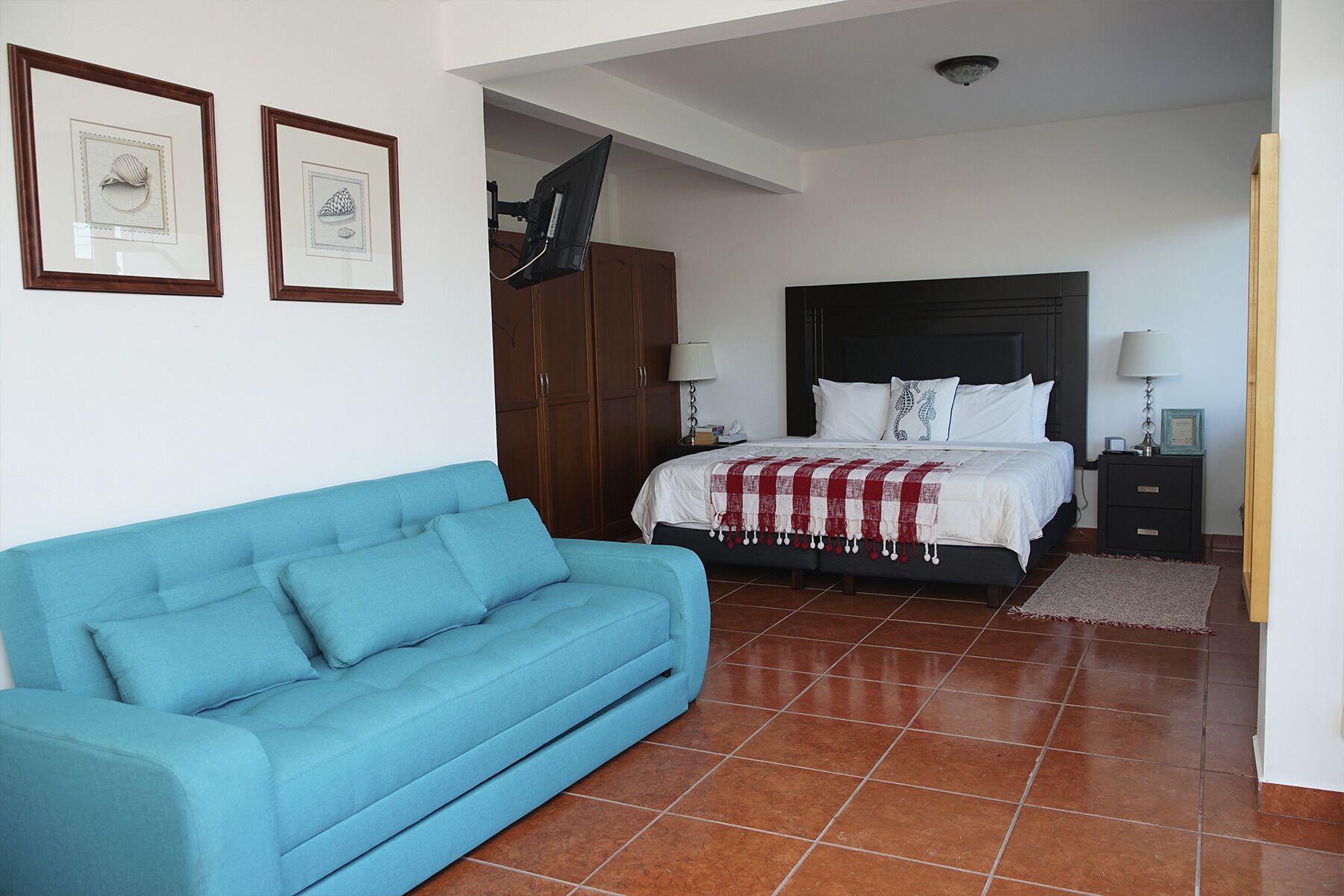 Un dormitorio con una cama, un sofá azul y dos cuadros enmarcados en la pared.
