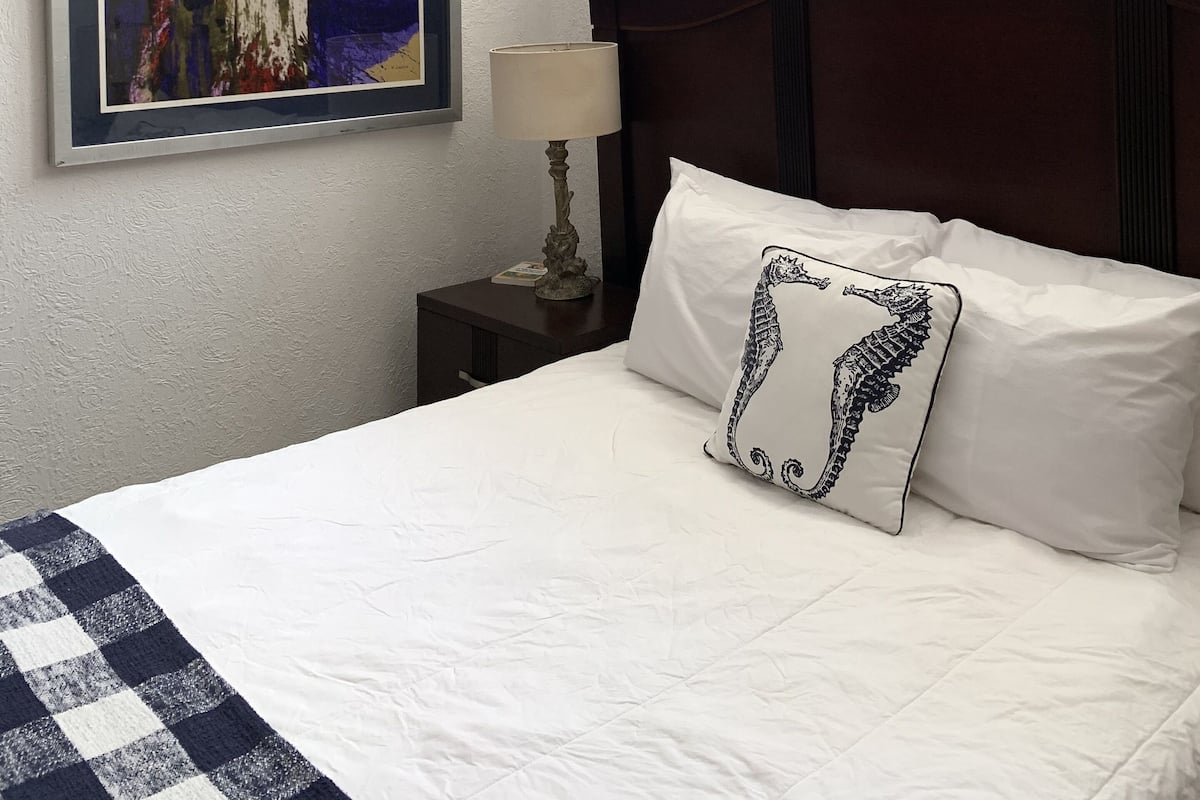 Une chambre d’hôtel avec un grand lit, une œuvre d’art encadrée au mur, une table de chevet avec une lampe et une fenêtre donnant sur un beau paysage.