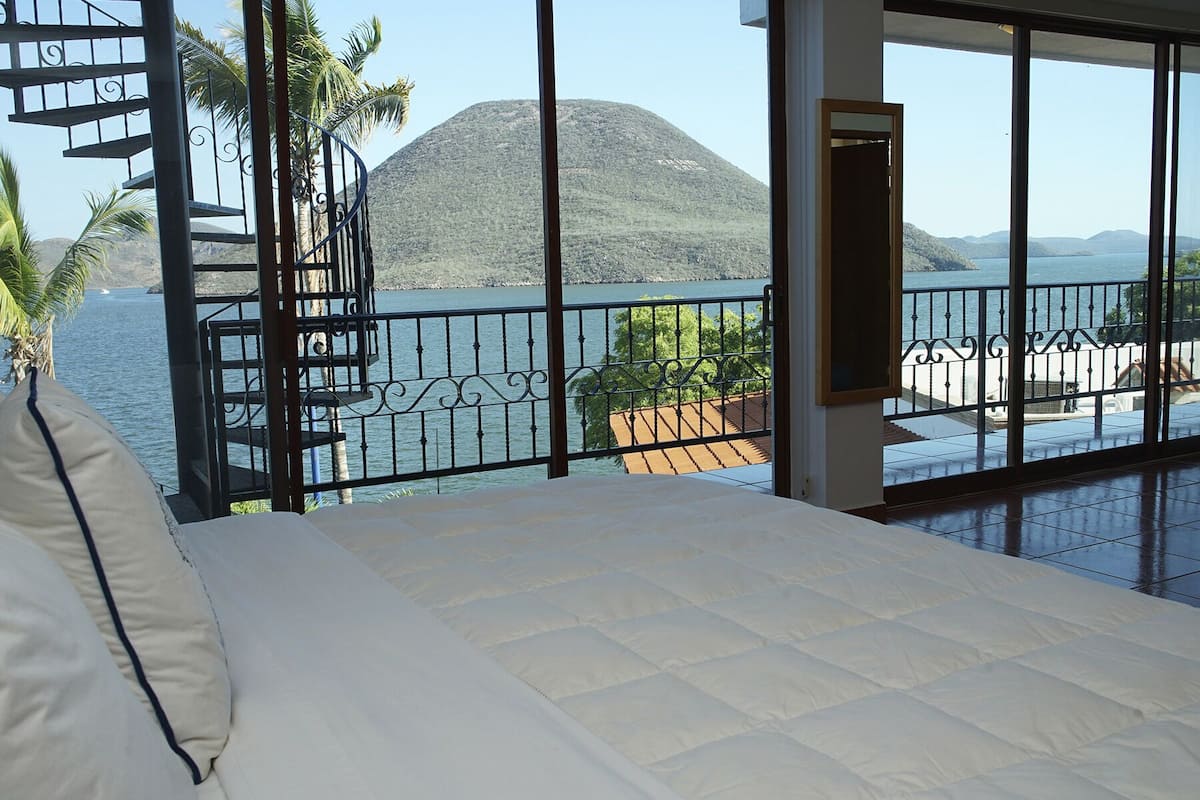 Une chambre avec un grand lit, une vue sur un plan d’eau et un balcon doté d’une balustrade.