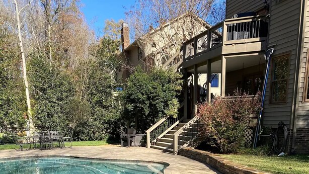 Una piscina cristallina con bordo in pietra, un solarium in legno e una scala che conduce a un balcone.