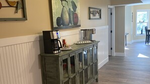 Un corridoio con un tavolo consolle in legno, una macchina da caffè e un dipinto di frutta appeso al muro.