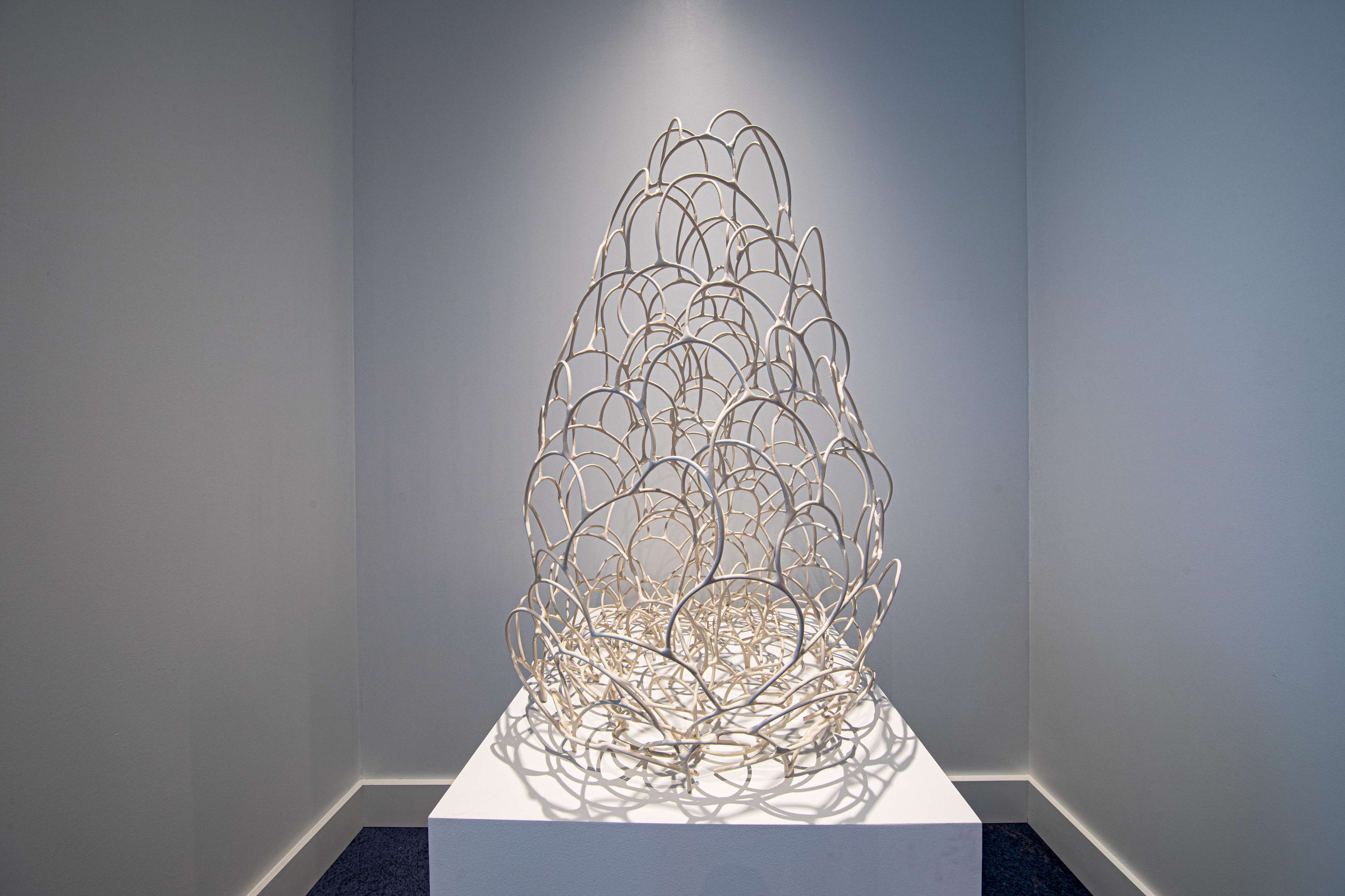 A metal sculpture on a pedestal in a gallery setting.
