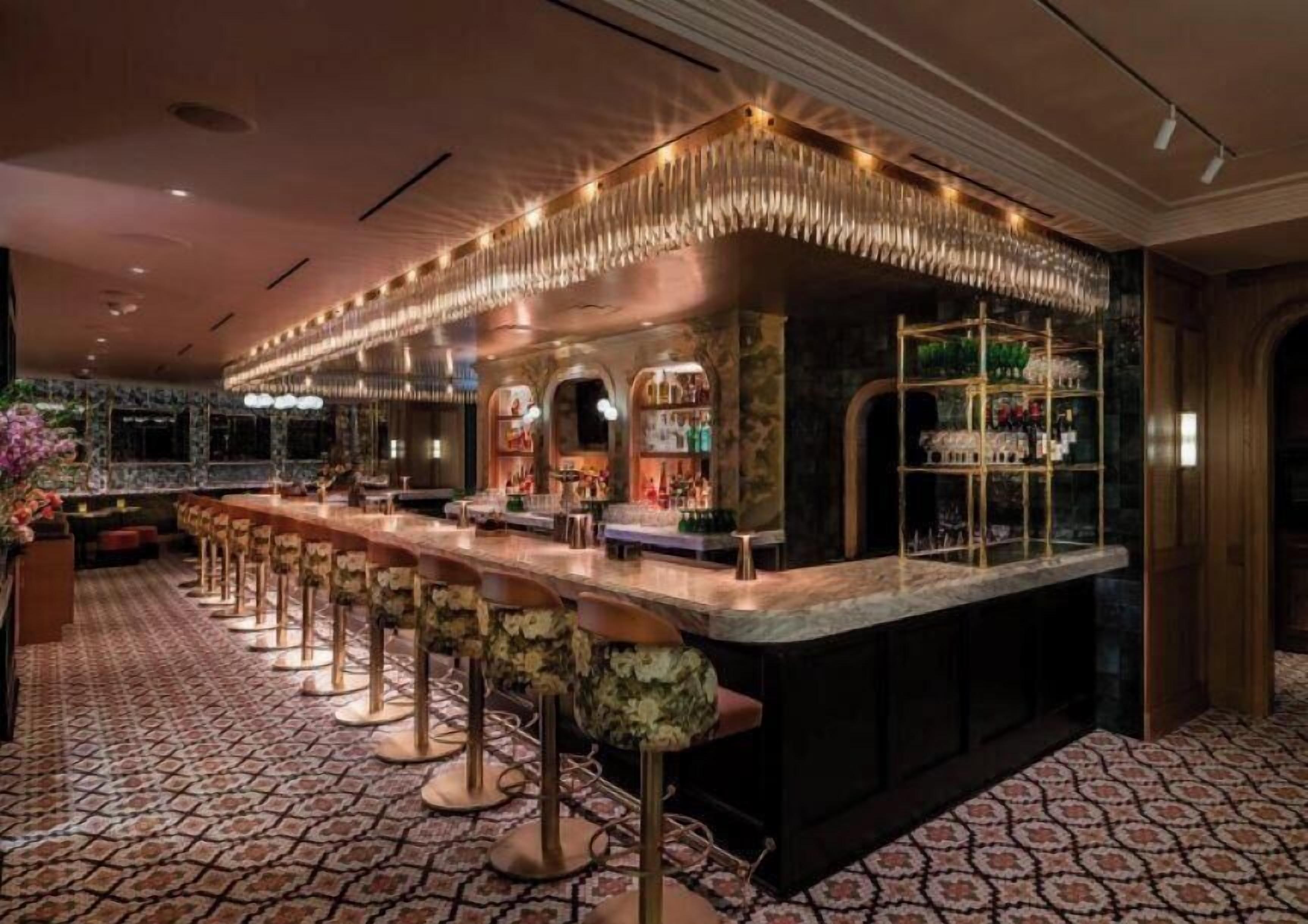 A bar area with a long counter, stools, and a decorative ceiling.
