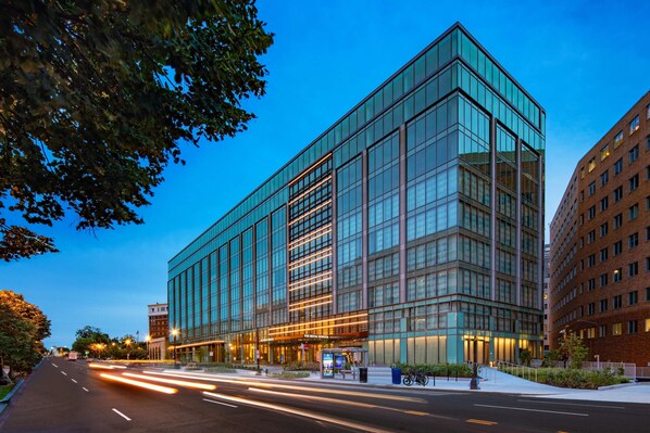 Un bâtiment moderne doté d’une façade en verre, d’une entrée imposante et d’une rue bien éclairée au premier plan.
