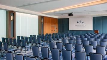 A conference room with rows of chairs, a podium, and a screen displaying "The Royal Sonesta Washington DC Capitol Hill".