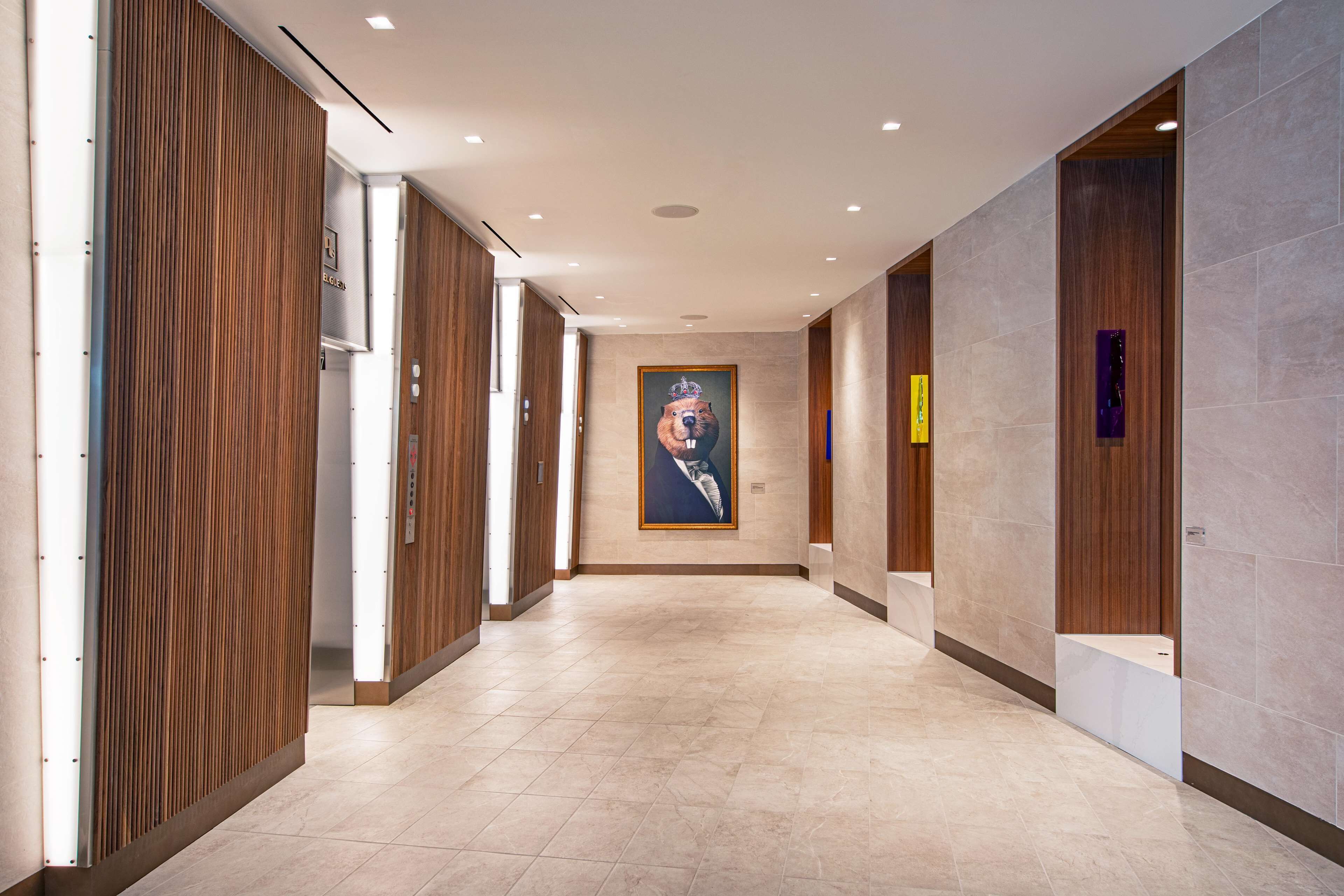 Un couloir d’hôtel moderne avec des lambris en bois, un grand tableau représentant un ours et un sol carrelé.