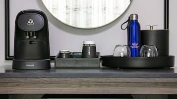 Ein modernes Badezimmer mit einer schwarzen Kaffeemaschine, einer blauen Wasserflasche und einem schwarzen Seifenspender auf einer Ablagefläche.