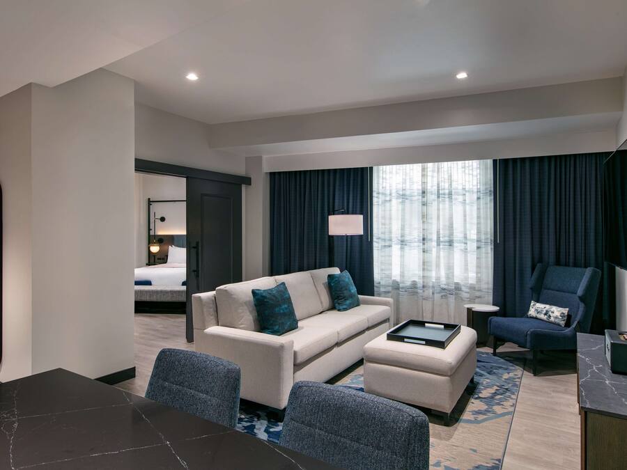A modern hotel room with a sofa, armchair, and a dining table.