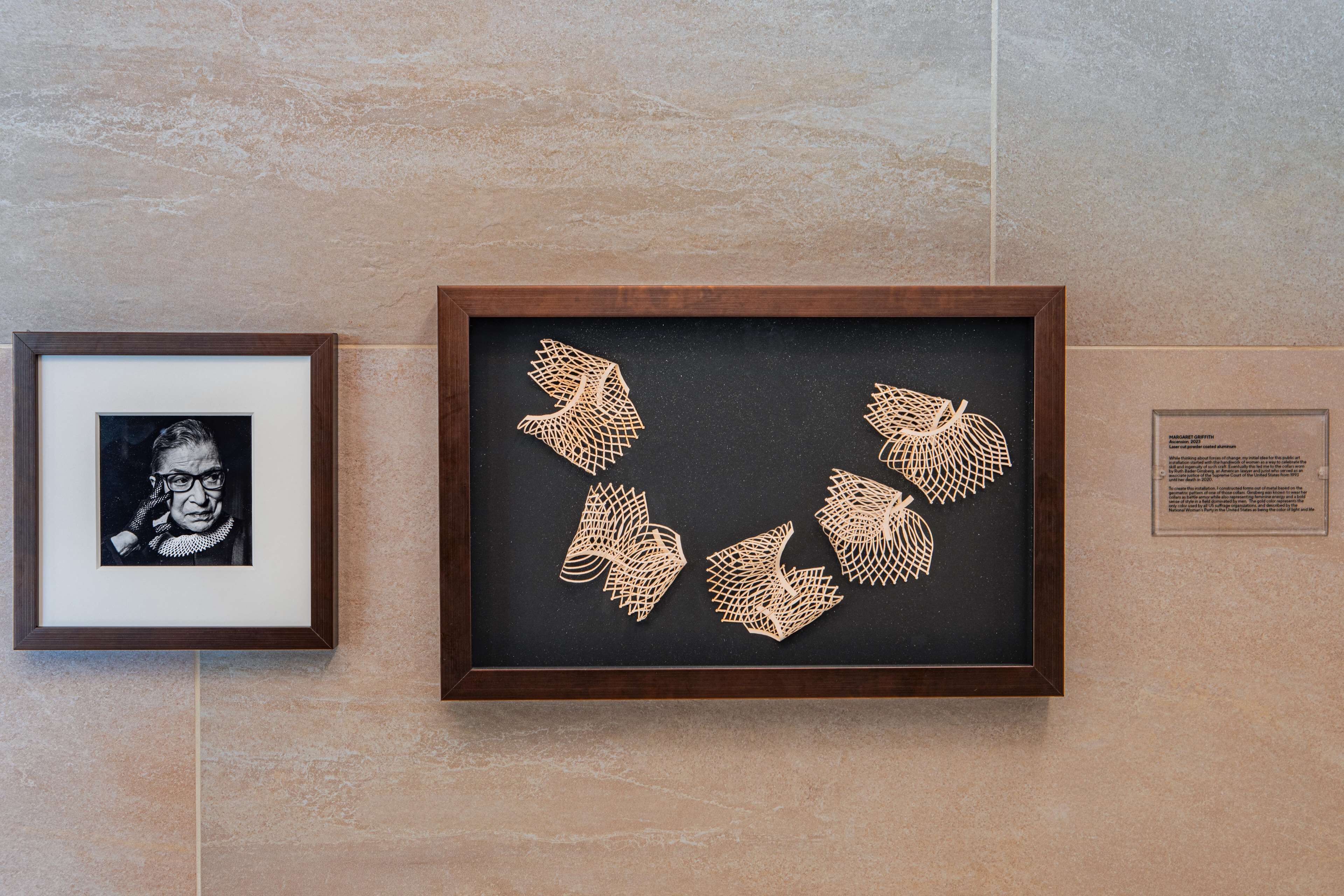 A framed artwork with geometric patterns on a black background, mounted on a wall with a tiled surface.