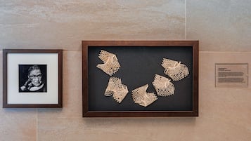 A framed artwork with geometric patterns on a black background, mounted on a wall with a tiled surface.