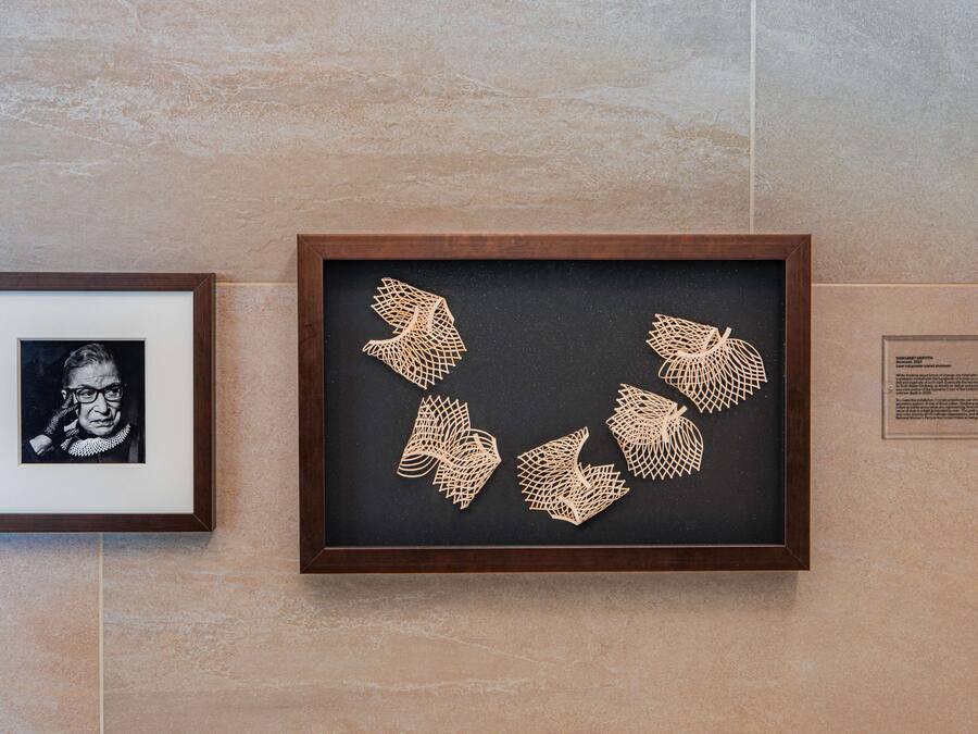 A framed artwork with geometric patterns on a black background, mounted on a wall with a tiled surface.