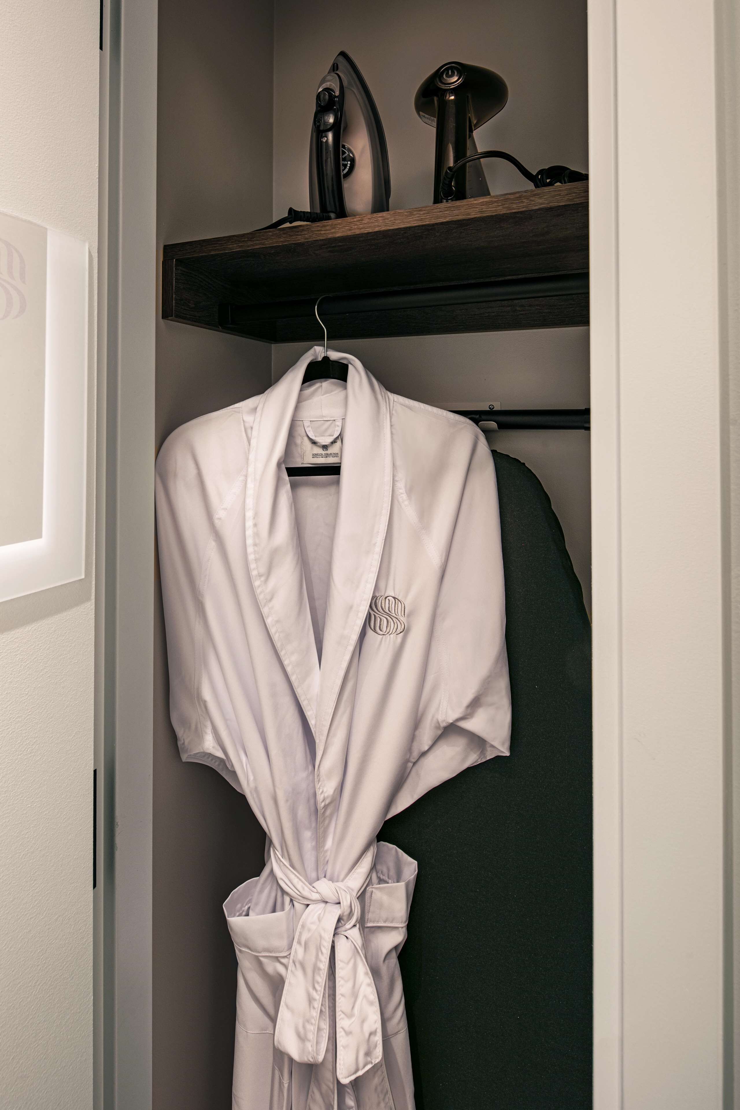 A white robe hanging on a rack in a closet with a wooden shelf above it.