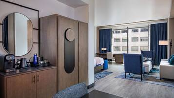 A hotel room with a bed, a desk, a chair, a sofa, a coffee maker, and a mirror.