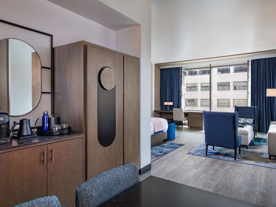 A hotel room with a bed, a desk, a chair, a sofa, a coffee maker, and a mirror.