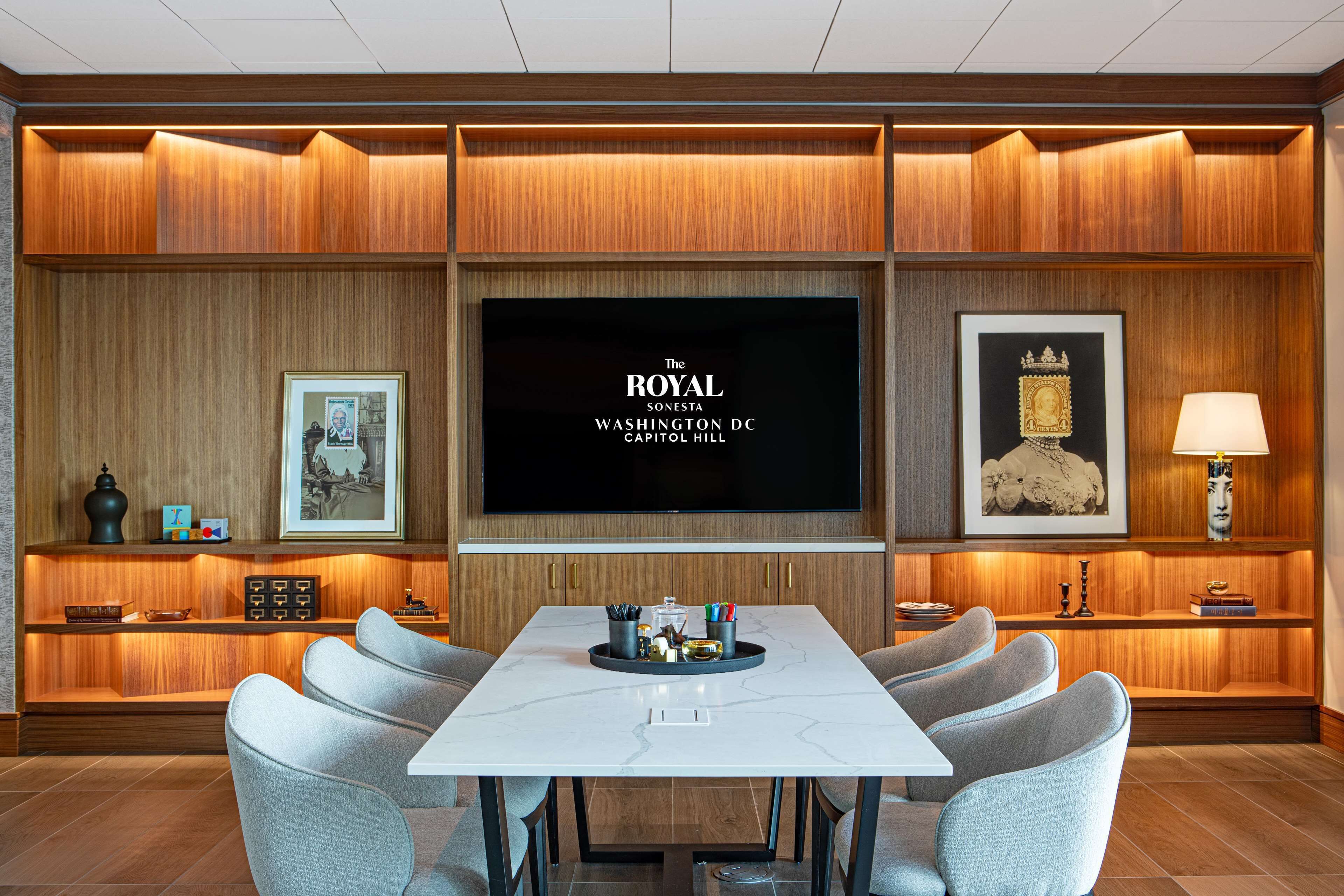 A conference room with a large table, multiple chairs, a flat-screen TV, framed artwork, and wooden paneling.