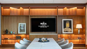 A conference room with a large table, multiple chairs, a flat-screen TV, framed artwork, and wooden paneling.