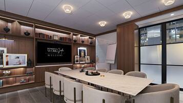 A modern conference room with a long table, comfortable chairs, a large screen, and a bookshelf with books and decorative items.