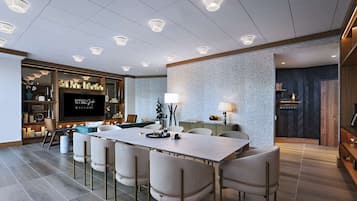 Een moderne hotelkamer met een grote eettafel, comfortabele zithoek, een flatscreen televisie en een gezellige zithoek met open haard.