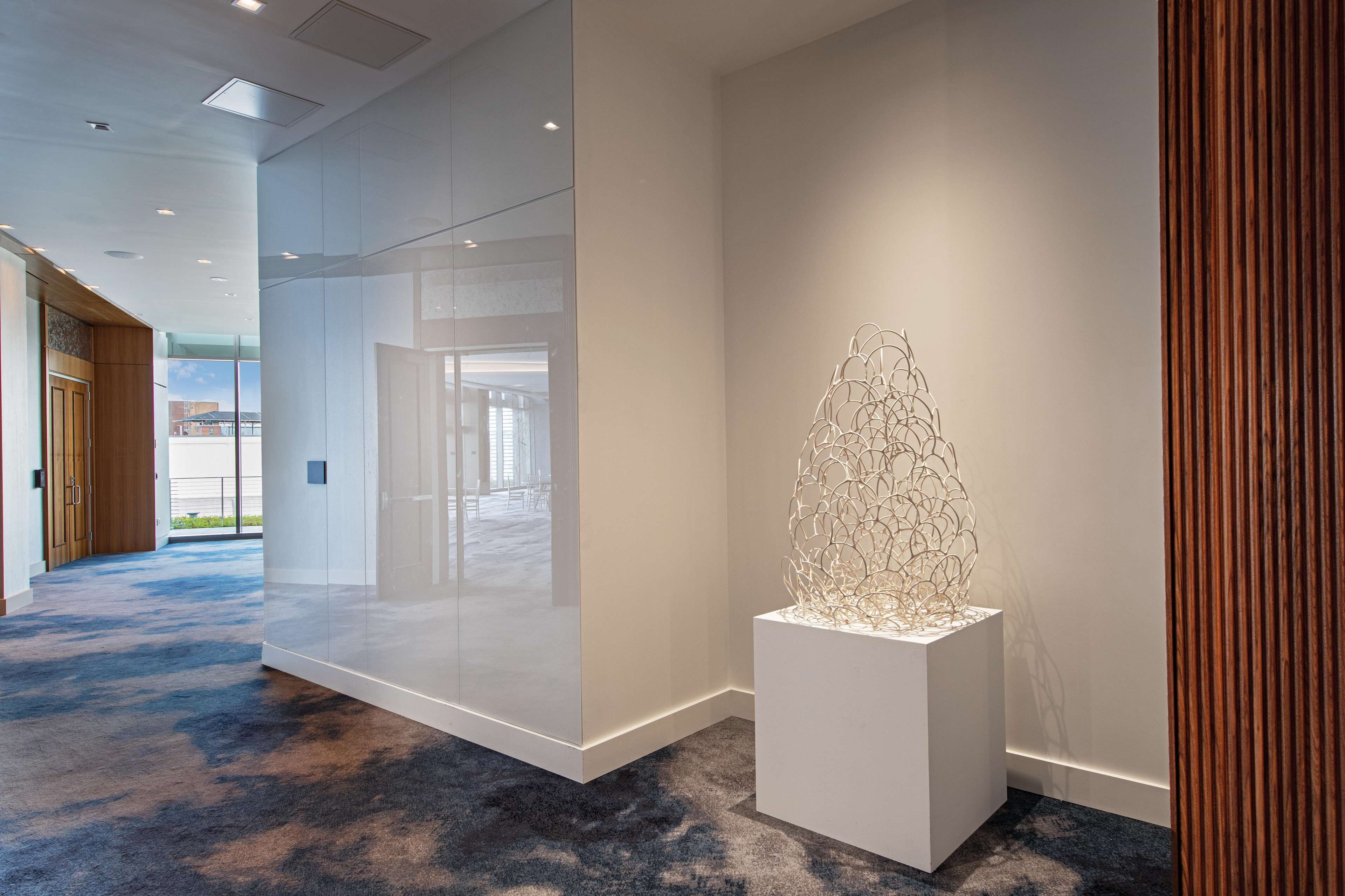 Un moderno vestíbulo de hotel con un separador de vidrio, una escultura blanca y una alfombra azul.